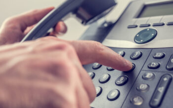 Man dialling out on a landline telephone pressing the number 6 with his finger on the keypad in a communications concept, close up of his hand and the instrument. With retro filter effect.