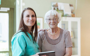 Portrait of smiling senior woman and nurse with digital tablet at home